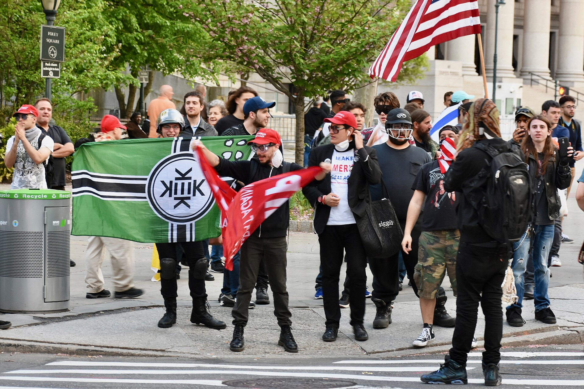 The Kekistan flag held open at the May Day demonstrations, Foley Square, New York, 1 May 2017. The flag is a parody of the Nazi-era German war ensign, with green in place of red, the 4chan logo in place of the Iron Cross, and a KEK device in place of the swastika. Photo: Alec Perkins, CC BY 2.0, via Wikimedia Commons.